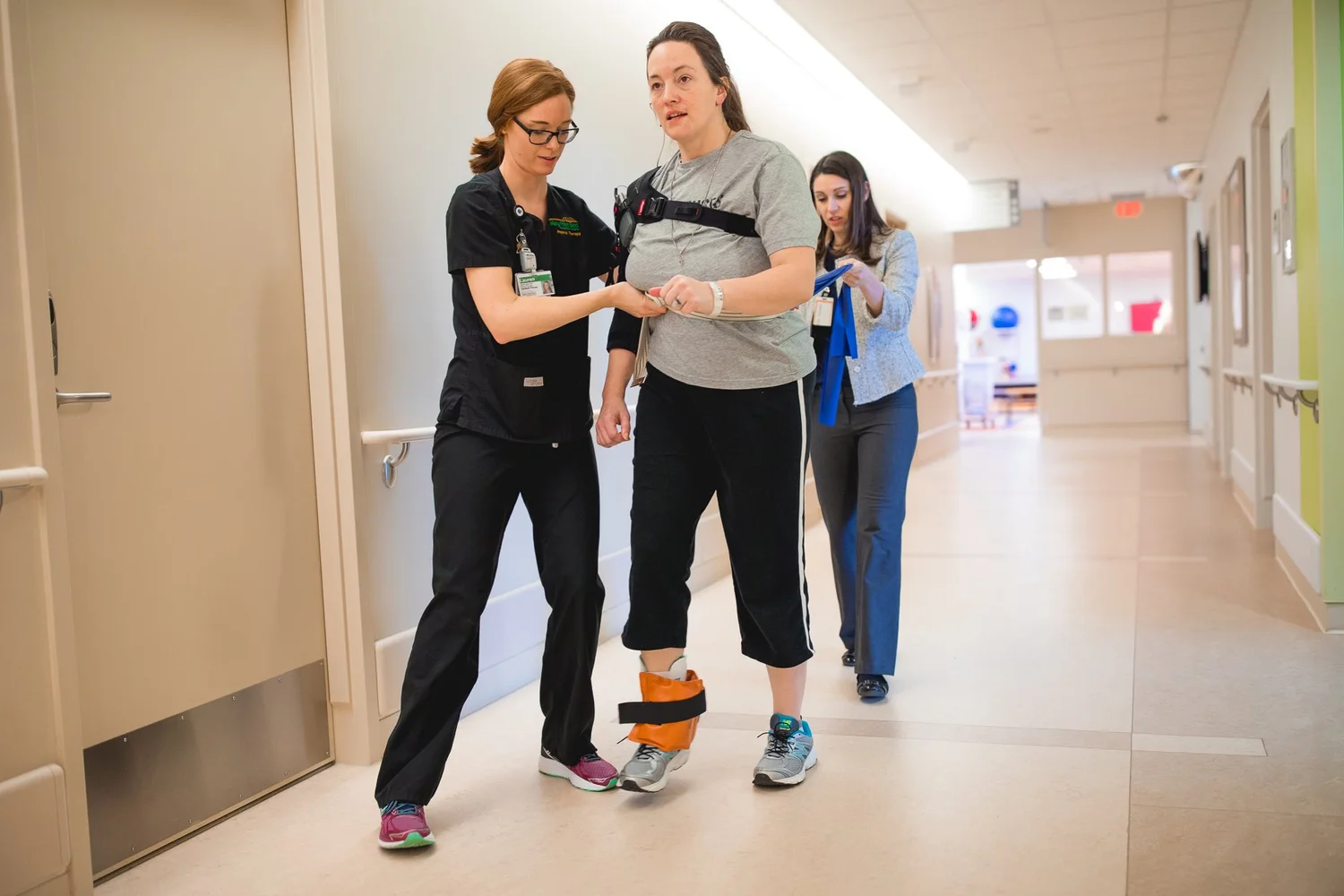 Physical therapy session with a patient and two therapists in a hospital corridor.